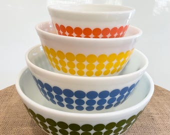 May include: Set of four nesting mixing bowls with a retro design. The bowls are white with a band of colorful polka dots in orange, yellow, blue, and green.