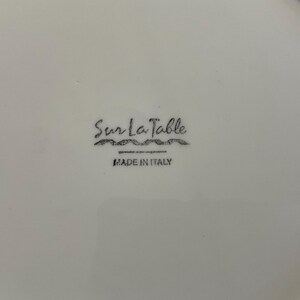 Puede incluir: Plato de cer&aacute;mica blanca con el logotipo de Sur La Table y el texto "MADE IN ITALY" en negro. El logotipo es una escritura estilizada con una l&iacute;nea ondulada debajo.