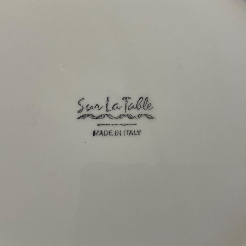 Puede incluir: Plato de cer&aacute;mica blanca con el logotipo de Sur La Table y el texto "MADE IN ITALY" en negro. El logotipo es una escritura estilizada con una l&iacute;nea ondulada debajo.
