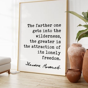 May include: A framed print with a gold frame displays a quote by Theodore Roosevelt: "The farther one gets into the wilderness, the greater is the attraction of its lonely freedom." The print is in a room with terracotta vases.