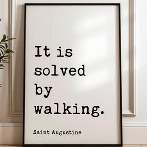 May include: Black and white typography print with the quote "It is solved by walking." attributed to Saint Augustine.
