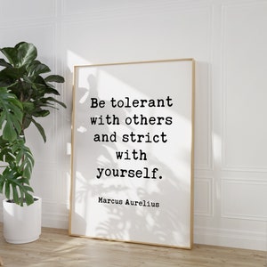 May include: A black and white typography print with a gold frame. The print features the quote "Be tolerant with others and strict with yourself." by Marcus Aurelius.