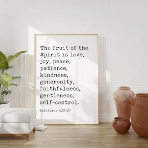 May include: A framed print with the text "The fruit of the Spirit is love, joy, peace, patience, kindness, generosity, faithfulness, gentleness, self-control. Galatians 5:22-23." The print is in a white frame and is displayed in a room with neutral tones.