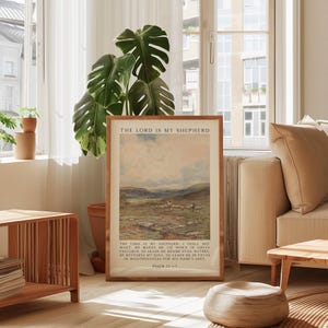 May include: A framed print with the text "THE LORD IS MY SHEPHERD" at the top. The artwork depicts a landscape with a flock of sheep. The bottom of the print includes text from Psalm 23:1-3. The frame is a light brown color.