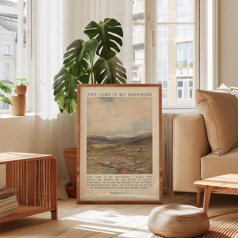 May include: A framed print with the text "THE LORD IS MY SHEPHERD" at the top. The artwork depicts a landscape with a flock of sheep. The bottom of the print includes text from Psalm 23:1-3. The frame is a light brown color.