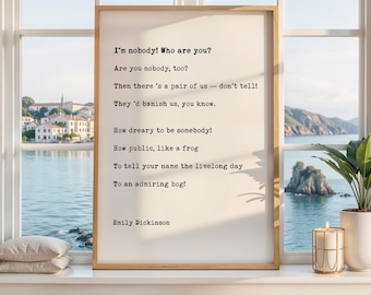 May include: A rectangular framed print featuring the poem I'm nobody! Who are you? by Emily Dickinson in black typewriter-style font on a cream background. The text is clearly legible, centred, and presented in a simple wooden frame.