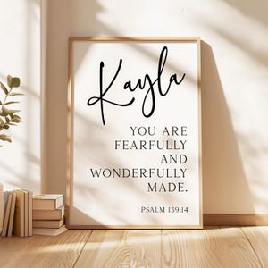 May include: A rectangular wall art print in a light wood frame featuring the name Kayla in a large black script font, followed by the text YOU ARE FEARFULLY AND WONDERFULLY MADE and the citation PSALM 139:14 in a clean black serif typeface.