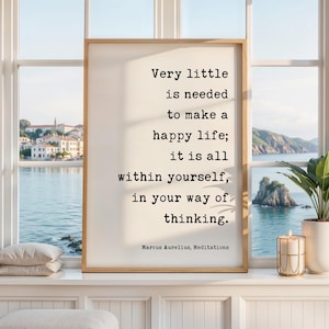 May include: A framed wall art print featuring the black text: Very little is needed to make a happy life; it is all within yourself, in your way of thinking. Marcus Aurelius, Meditations. The print has a light cream background and a wooden frame.