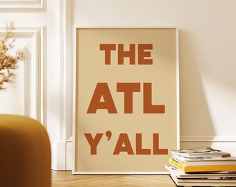 May include: A rectangular framed wall art print featuring a light beige background with bold, dark orange sans-serif text that reads THE ATL Y'ALL. The print is displayed in a simple white frame, showcasing a clean and modern typographic design.