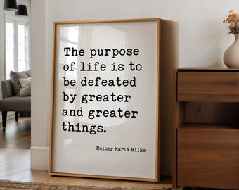 Può includere: Un quadro rettangolare con testo nero in stile macchina da scrivere su sfondo bianco che recita, The purpose of life is to be defeated by greater and greater things. - Rainer Maria Rilke, racchiuso in una cornice di legno chiaro.