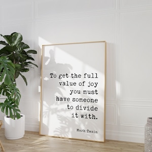 May include: A rectangular framed wall art print featuring black typewriter-style text on a white background that reads: To get the full value of joy you must have someone to divide it with. Mark Twain. The frame is a light-colored wood finish.