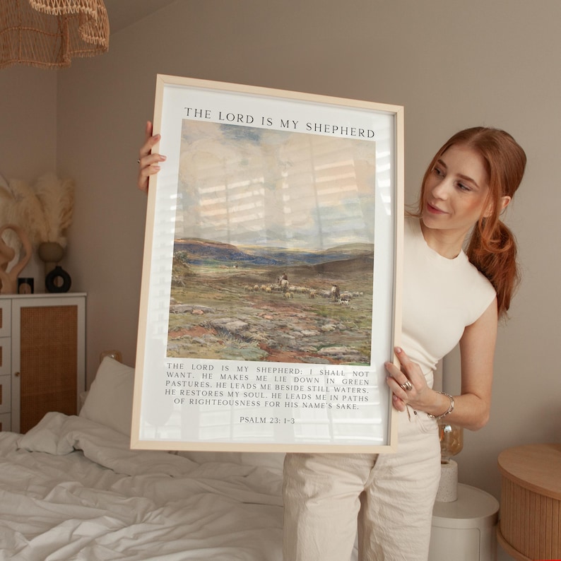 May include: Framed art print featuring a pastoral landscape with sheep, mountains, and a cloudy sky. The text "THE LORD IS MY SHEPHERD" is at the top, with Psalm 23:1-3 below. The frame is light-colored.