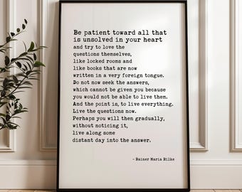 Pode incluir: Um quadro retangular com moldura preta apresentando texto preto em estilo de máquina de escrever sobre um fundo branco. O texto diz: Be patient toward all that is unsolved in your heart and try to love the questions themselves, assinado Rainer Maria Rilke.
