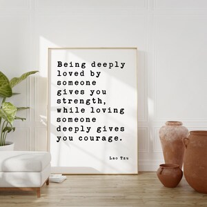 May include: A rectangular framed wall art print featuring black typewriter-style text on a white background. The quote reads: Being deeply loved by someone gives you strength, while loving someone deeply gives you courage. The author is Lao Tzu.