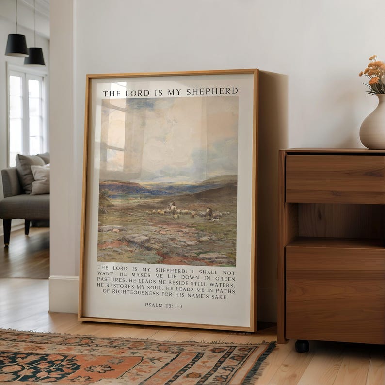 May include: A framed print with a landscape scene and the text "THE LORD IS MY SHEPHERD." The artwork depicts a shepherd with sheep in a field. The text from Psalm 23:1-3 is below the image. The frame is a light brown color.