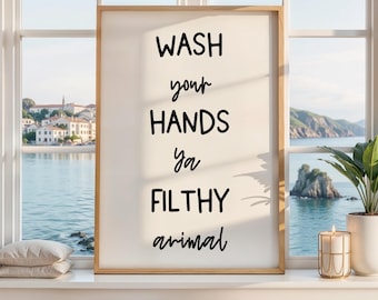 May include: A vertical rectangular wall art print in a light wood frame featuring the black text WASH your HANDS ya FILTHY animal centered on a cream background. The typography alternates between bold block letters and a cursive script style.
