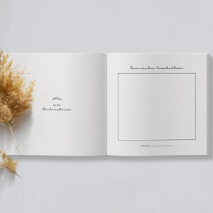May include: An open, off-white journal with the text "Deine Meilensteine" and a drawing of a rabbit. The right page has a blank box with the text "Dein erster Haushalt" above it and "Datum" below. A dried, tan plant is on the left.