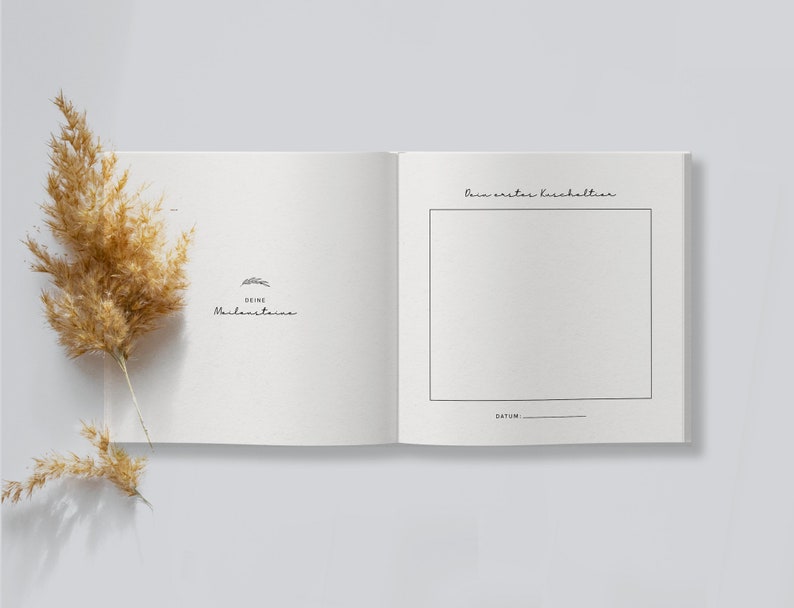May include: An open, off-white journal with the text "Deine Meilensteine" and a drawing of a rabbit. The right page has a blank box with the text "Dein erster Haushalt" above it and "Datum" below. A dried, tan plant is on the left.