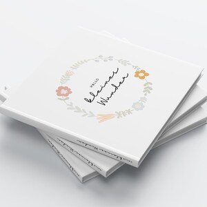 May include: A stack of white books with a floral wreath design and the text "Hallo kleines Wunder" on the cover.