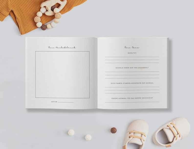 May include: An open baby memory book with text in German, featuring pages for handprints and name details. The book is surrounded by baby shoes, a wooden toy, and other baby accessories.