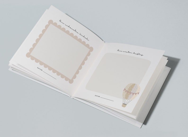 May include: An open baby memory book with two blank pages. The left page has a scalloped frame with the text "Dein wahrer erster Lacher" and the right page has a hot air balloon illustration with the text "Dein erster Ausflug". Both pages have a blank space for a date.
