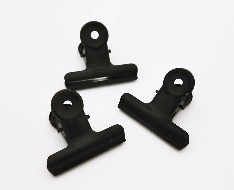 May include: Three black metal binder clips. The clips are closed and have a spring mechanism.