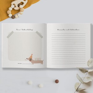 May include: A white book with a brown dachshund wearing a party hat and holding candles. The book has the text "Dein 1. Geburtstag" on the left page and "W&uuml;nsche und Gedanken" on the right page.