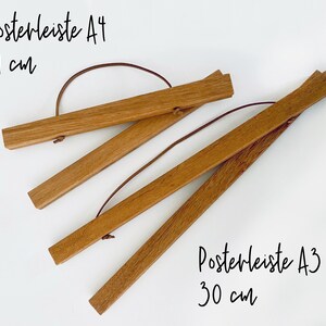 May include: Two wooden poster hangers, one for A4 size (21 cm) and one for A3 size (30 cm). The hangers are made of natural wood and have a leather strap.
