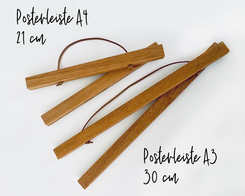 May include: Two wooden poster hangers, one for A4 size (21 cm) and one for A3 size (30 cm). The hangers are made of natural wood and have a leather strap.