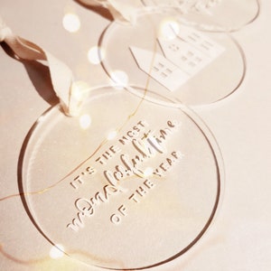 May include: Three clear acrylic Christmas ornaments with white lettering. One ornament says "It's the most wonderful time of the year".