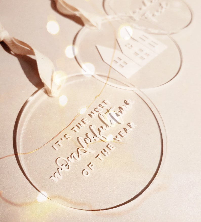 May include: Three clear acrylic Christmas ornaments with white lettering. One ornament says "It's the most wonderful time of the year".