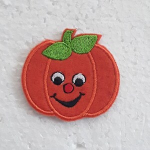Peut inclure: Une citrouille orange souriante avec une tige verte et des yeux noirs. La citrouille a un nez rouge et une bouche noire.