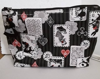 Può includere: Borsa a zip nera e bianca con un motivo ripetitivo di carte da gioco, orologi e personaggi di Alice nel Paese delle Meraviglie. La borsa ha uno sfondo a righe bianco e nero.