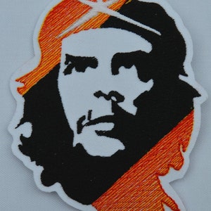 Op de afbeelding: Zwart-witte geborduurde afbeelding van Che Guevara met een rood-oranje gestreepte achtergrond. De afbeelding is 11 1/8 inch breed.