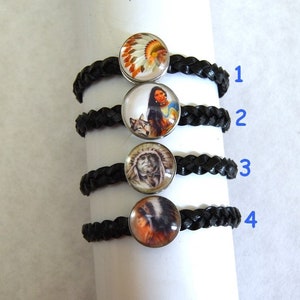 Pode incluir: Quatro pulseiras de couro trançado preto com diferentes cabochões de vidro com tema nativo americano. Os cabochões apresentam imagens de um nativo americano com um cocar, uma mulher nativa americana com um lobo, um homem nativo americano com um cocar e uma mulher nativa americana com um cocar. As pulseiras são numeradas de 1 a 4.