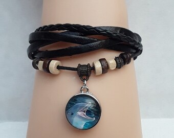 Può includere: Un braccialetto in pelle nera con perline di legno marrone e un ciondolo d'argento con l'immagine di un delfino.