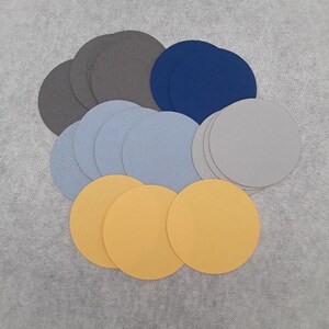 Puede incluir: Surtido de círculos de papel en varios tamaños y colores, incluyendo gris, azul, azul claro, amarillo y blanco.