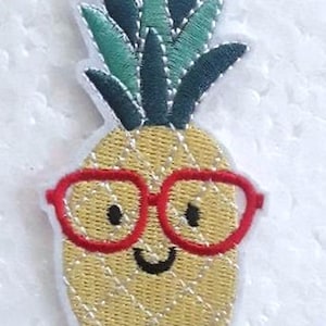 Op de afbeelding: Geborduurde strijkpatch van een gele ananas met een groene, bladerige bovenkant, die een rode bril draagt en lacht.