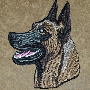 May include: Embroidered patch depicting a dog's head in profile, with tan and black thread detailing. The dog's mouth is open, displaying a pink tongue. The patch is intricately stitched, creating a textured effect. The design is suitable for various applications.