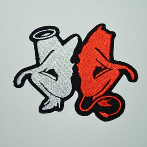 Könnte beinhalten: Gestickter Aufnäher mit einem weißen Engel und einem roten Teufel, beide mit Flügeln und Heiligenscheinen, in einer verspielten Pose ineinander verschlungen.