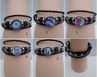 Può includere: Cinque braccialetti in pelle diversi con dettagli in metallo e una varietà di cabochon di vetro. I cabochon presentano immagini di un occhio, delfini, una farfalla, un lupo e un viso di donna.