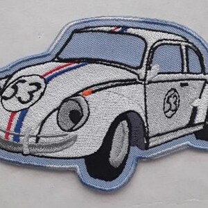 Può includere: Una toppa ricamata bianca di un'auto dei cartoni animati con un contorno blu. L'auto ha il numero "53" sul lato e una striscia blu, bianca e rossa sul cofano.