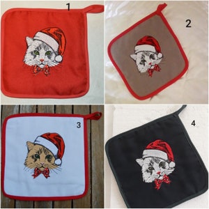 Könnte beinhalten: Vier unterschiedlich farbige Topflappen mit einem weißen Kätzchen, das einen Weihnachtsmann-Hut trägt, darauf gestickt. Die Topflappen sind rot, grau, weiß und schwarz.