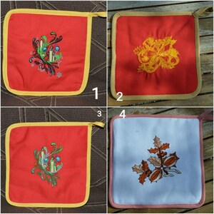 Op de afbeelding: Vier rode en witte ovenwanten met verschillende geborduurde kerstontwerpen. De ontwerpen omvatten een kaars, hulst en een strik.