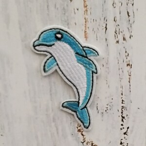 Peut inclure: Un patch brodé de dauphin bleu et blanc. Le dauphin est tourné vers la gauche et a un ventre blanc et un dos bleu. Le patch est parfait pour ajouter une touche de fantaisie à n'importe quel projet.