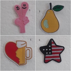 Peut inclure: Quatre patchs brodés thermocollants. Le premier patch est rose et représente une main souriante à deux doigts. Le deuxième patch est jaune et représente une poire avec une feuille verte. Le troisième patch est rouge et jaune et représente un cœur brisé avec une chope de bière. Le quatrième patch est noir et rouge et représente une étoile avec le motif du drapeau américain.