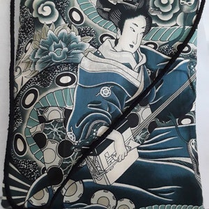May include: A blue and white drawstring bag with a Japanese-inspired design featuring a woman playing a musical instrument. The bag has a black drawstring and a black strap.