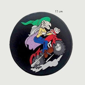 Puede incluir: Un parche bordado en blanco y negro de una bruja montando una motocicleta roja. La bruja lleva un sombrero verde y una túnica morada. La motocicleta tiene una estela de humo blanco detrás. El parche tiene 17 cm de diámetro.