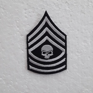 Op de afbeelding: Zwart-witte geborduurde patch met een schedel en vijf witte strepen op een zwarte achtergrond. De patch heeft de vorm van een chevron.