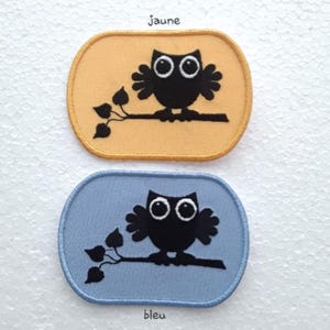 May include: Two iron-on patches featuring a black silhouette of an owl perched on a branch. The patches are oval shaped and have a yellow and blue background. The text "jaune" is above the yellow patch and "bleu" is below the blue patch.